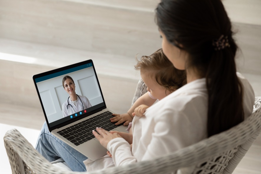 Mother with child sitting at home using a laptop to telemedicine