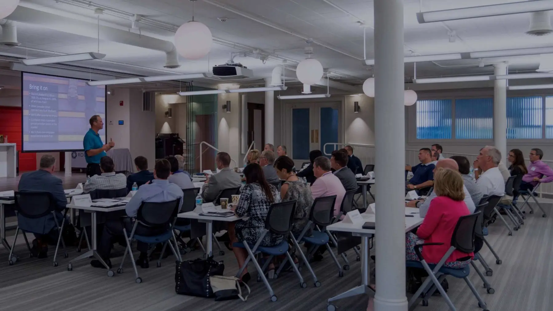 Attendees seated at tables watching a presenter during a conference session.