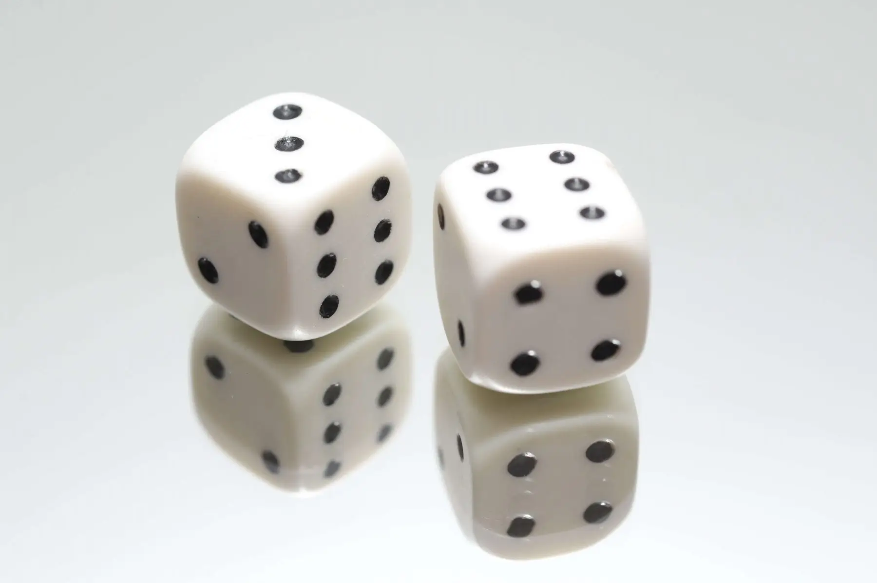 Two white dice on a reflective surface.