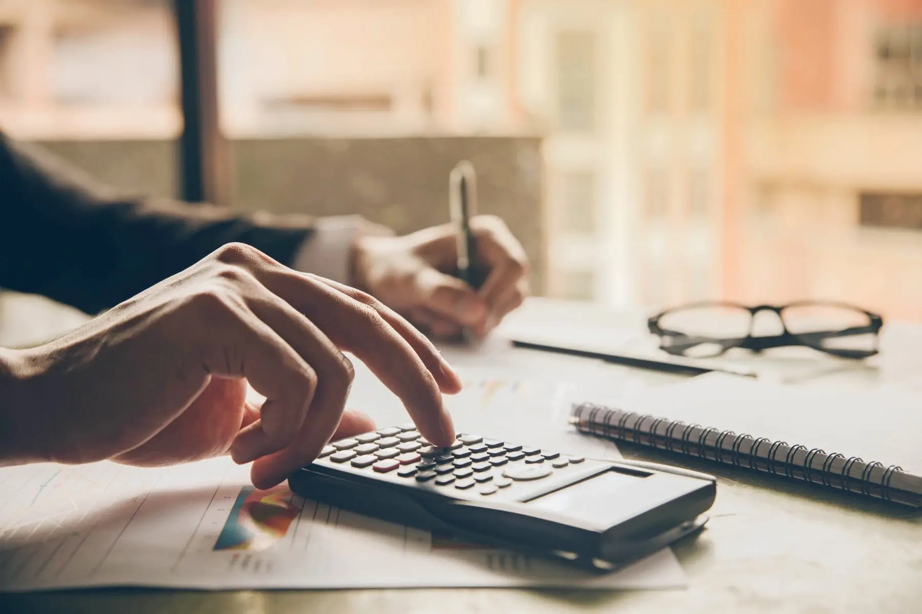 Close-up of a person using a calculator and writing notes at a desk.
