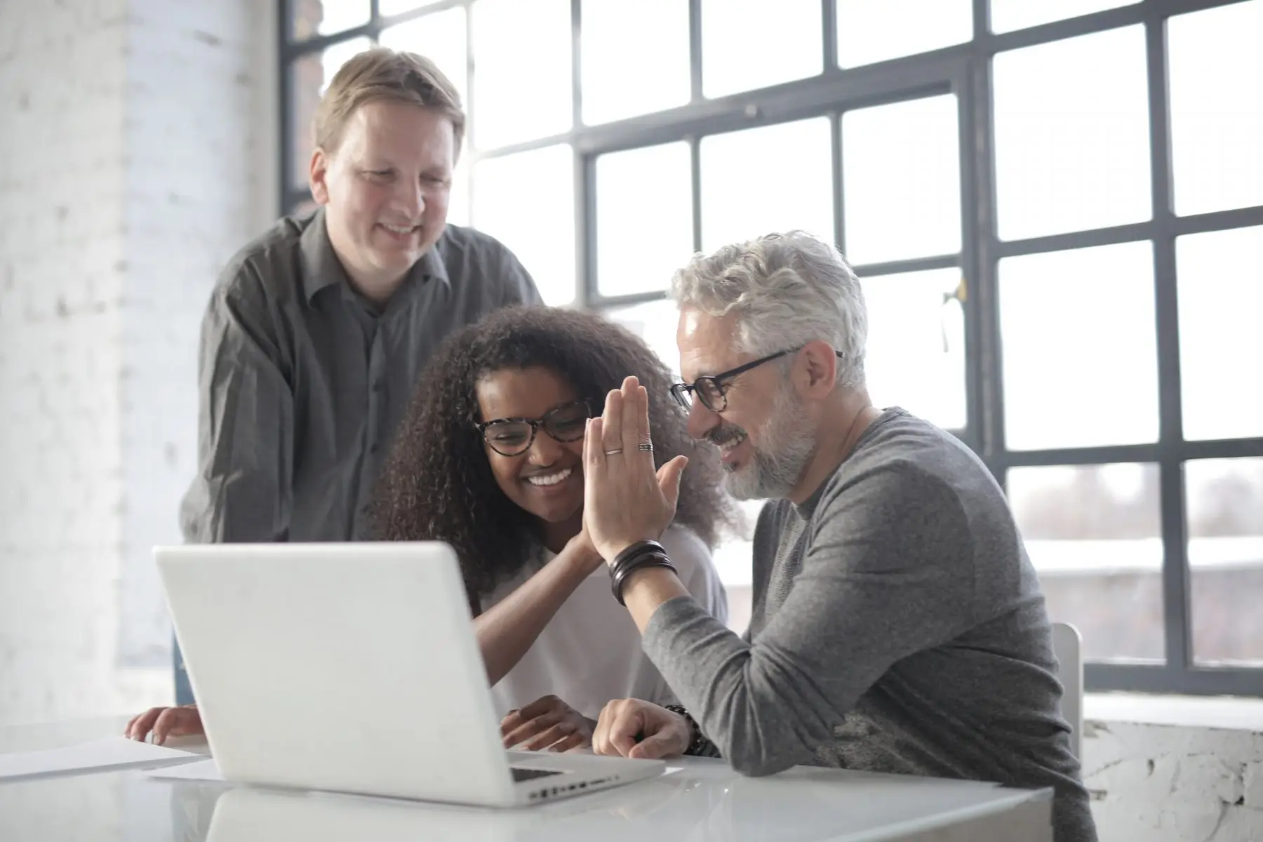 Three colleagues smiling around a laptop in a bright office.