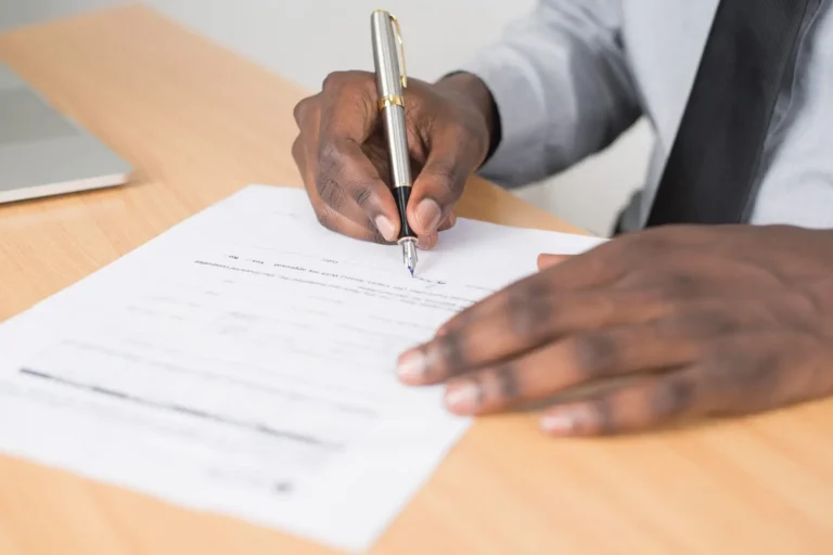 Close-up of a man signing a document with a pen at a desk.