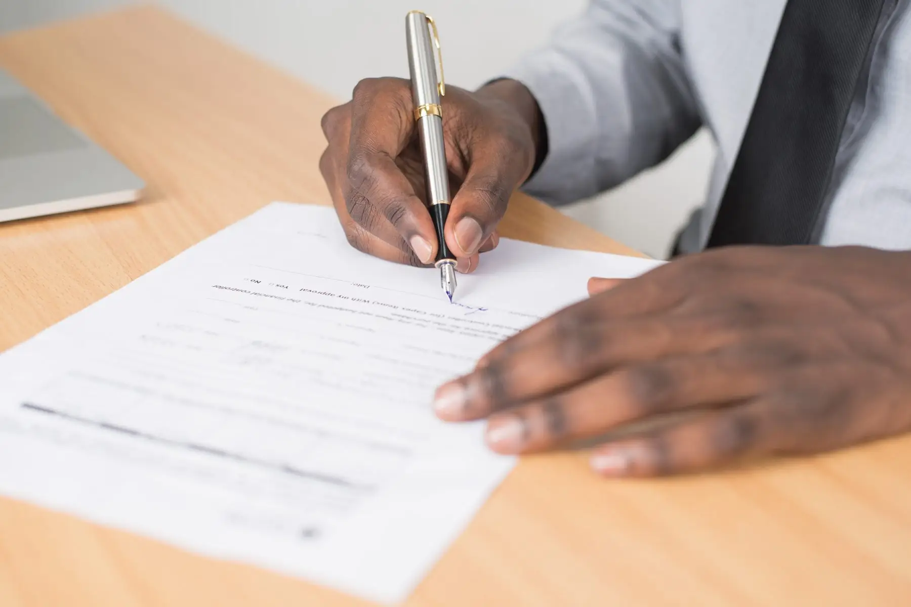 Close-up of a man signing a document with a pen at a desk.