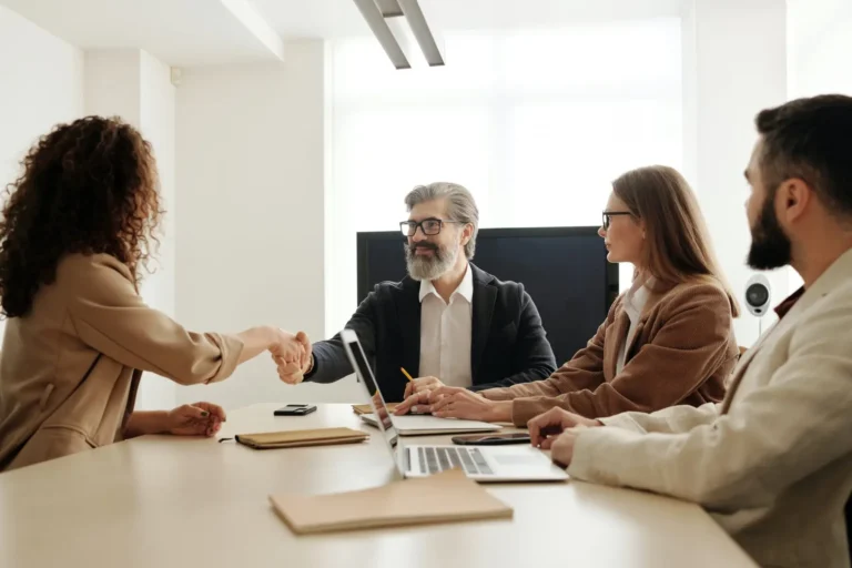 A woman shaking hands with a man across a conference table during a meeting.
