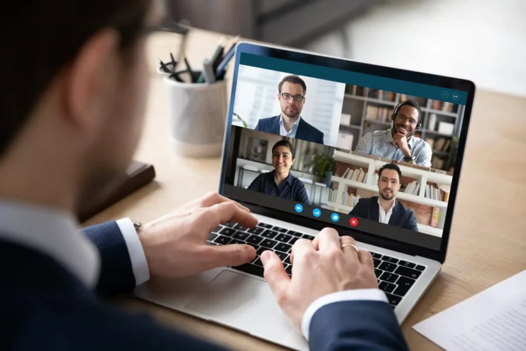 A man on a video call with three colleagues shown on his laptop.