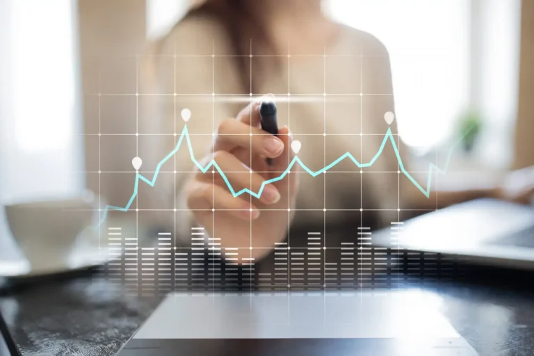 A woman marking a rising line graph over a laptop, representing data analytics.