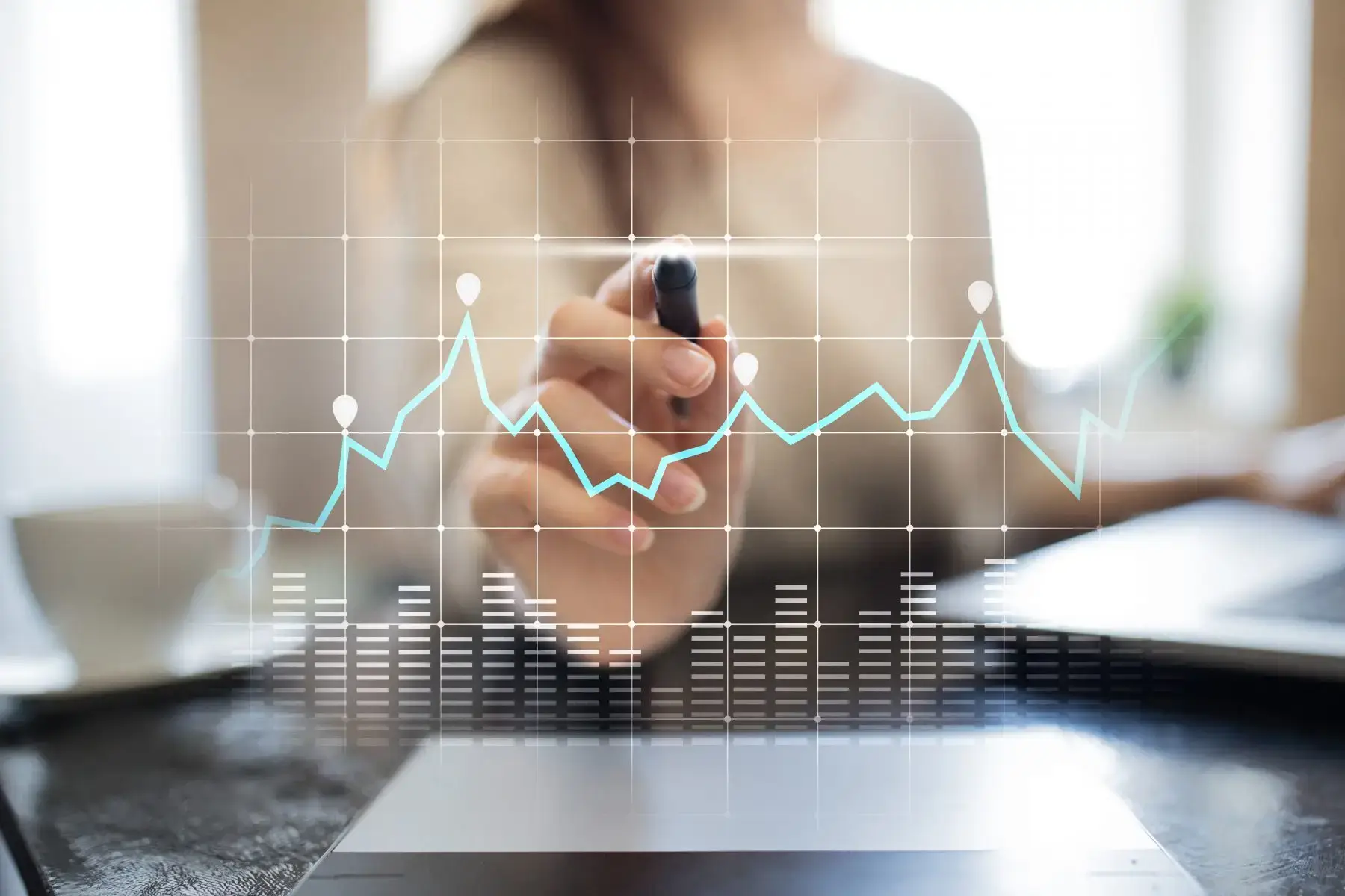 A woman marking a rising line graph over a laptop, representing data analytics.