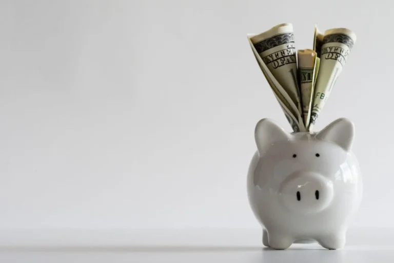 A white piggy bank with rolled dollar bills tucked into the top.