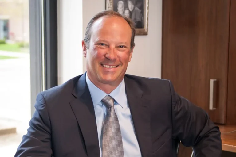 A smiling businessman in a suit seated by an office window.