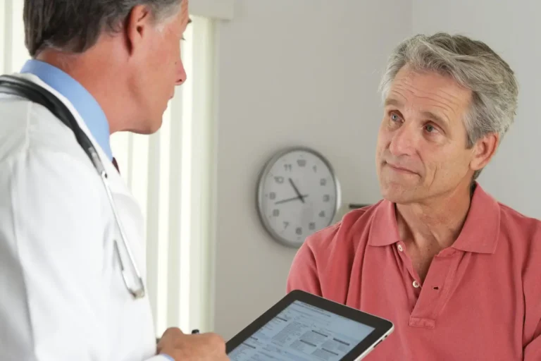 A doctor showing a tablet to a middle-aged male patient in an exam room.