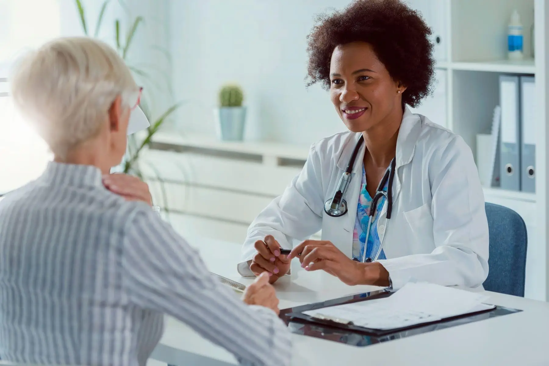 A smiling doctor talking with an older patient at a desk.