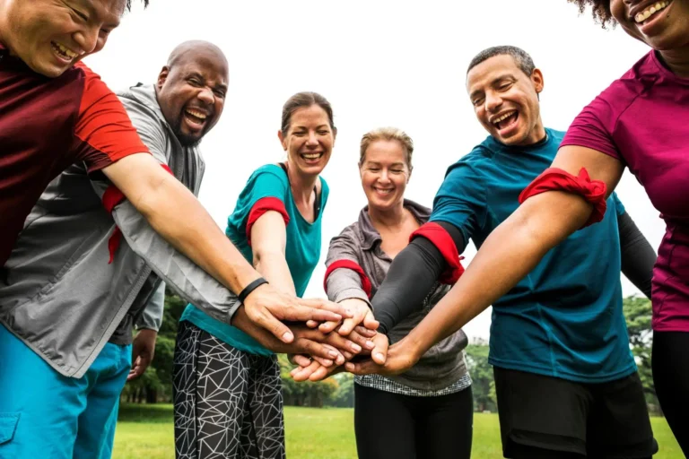 A diverse group in athletic wear joining hands in a huddle outdoors.