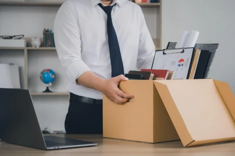 A man packing personal belongings into a cardboard box at his desk.