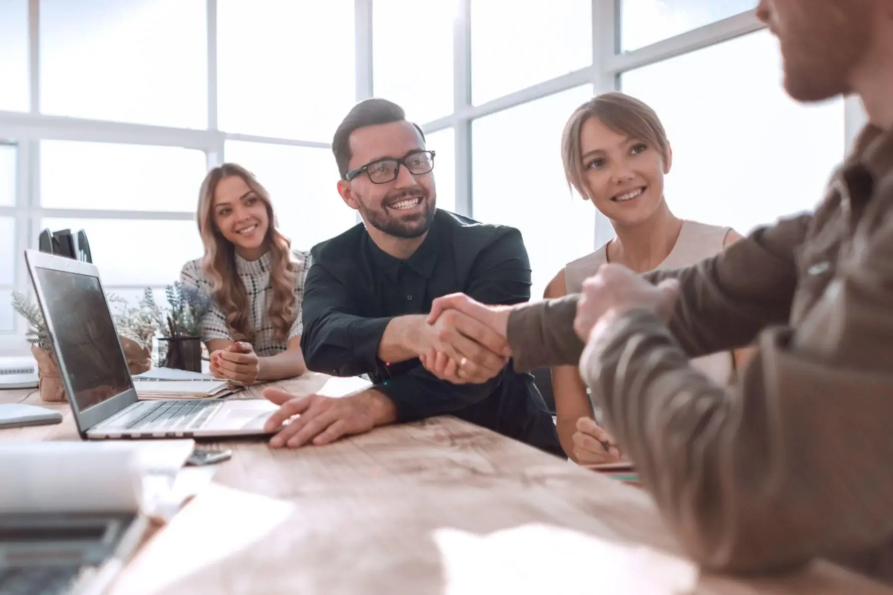 Colleagues smiling as two people shake hands across a table.
