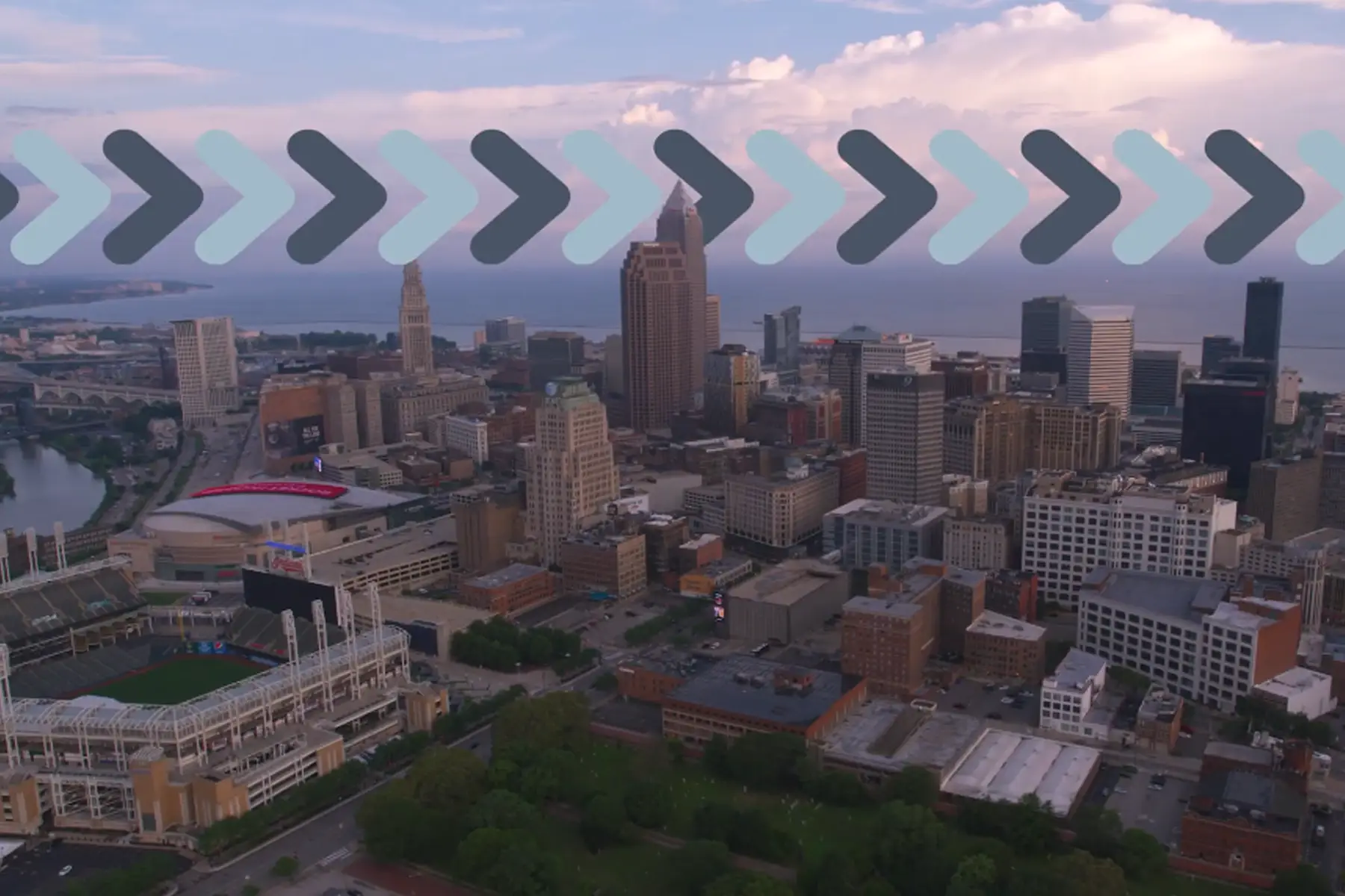 Aerial view of a downtown city skyline with a stadium, overlaid with an arrow motif.