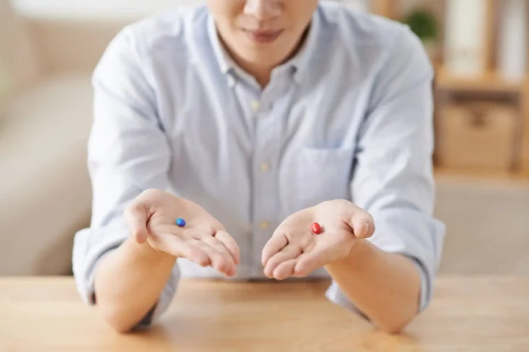 A man holding out a blue pill in one hand and a red pill in the other, representing a choice.