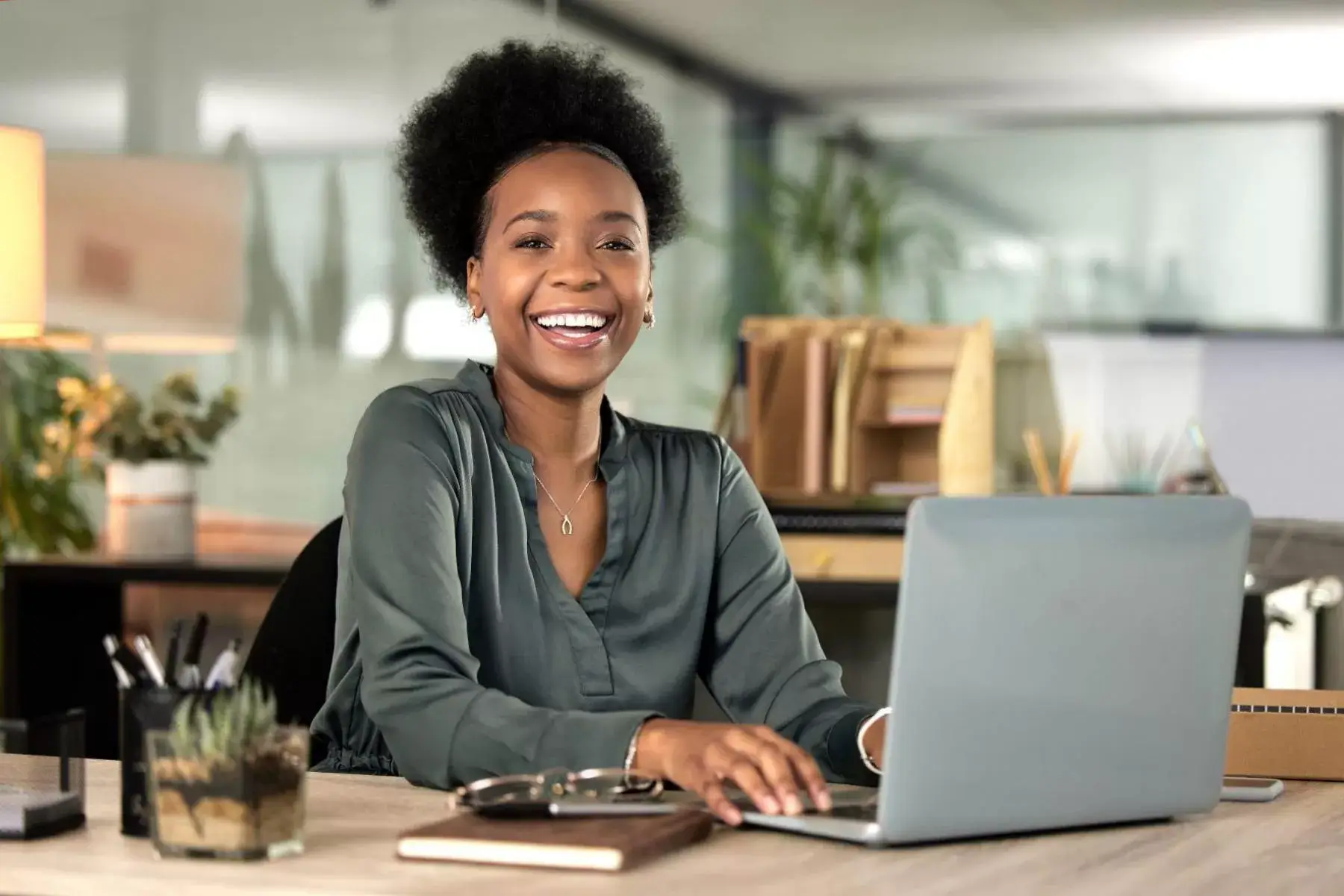 A smiling woman working at a laptop in a bright office.