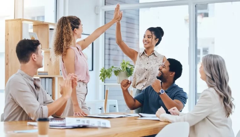 Team celebrating success with high-fives in a bright office meeting room