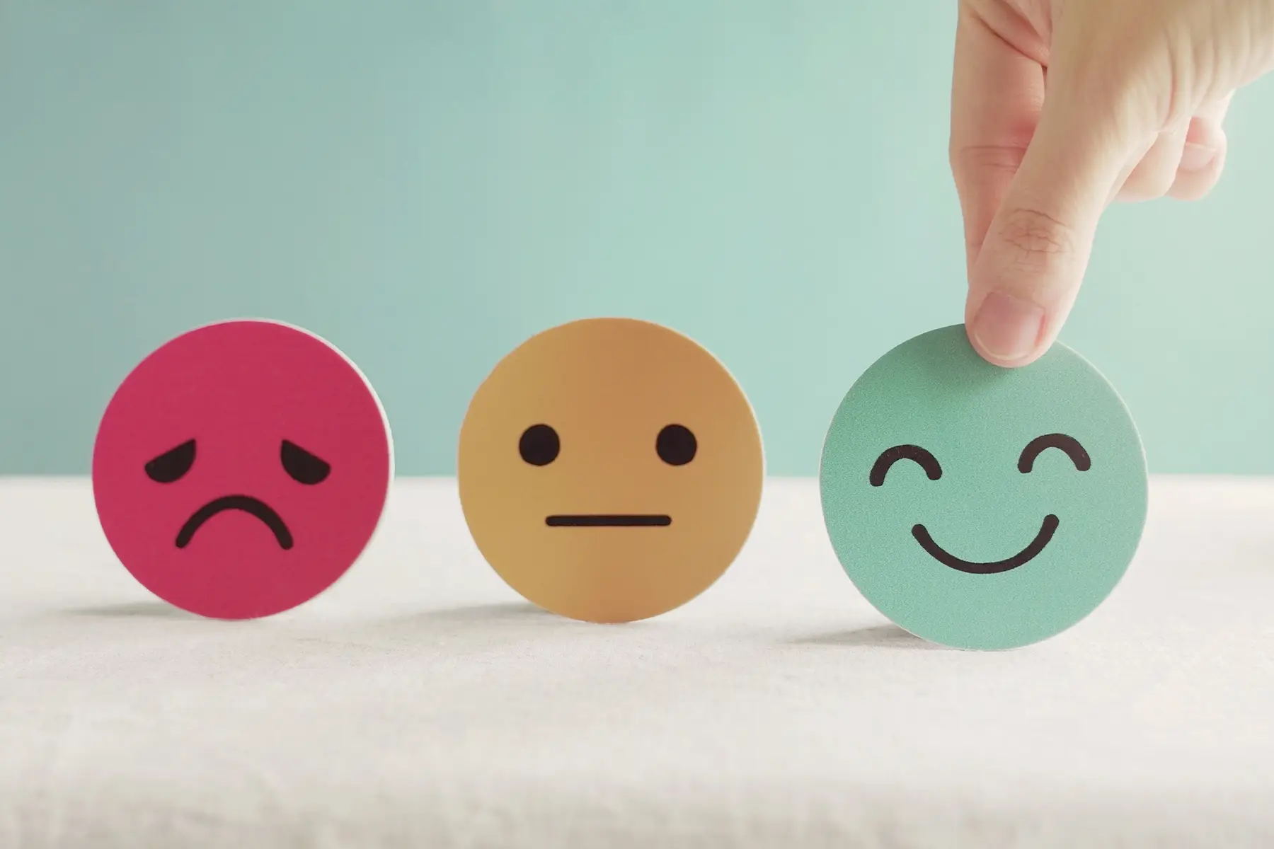 A hand selecting a smiling-face card from sad, neutral, and happy faces, representing customer satisfaction.
