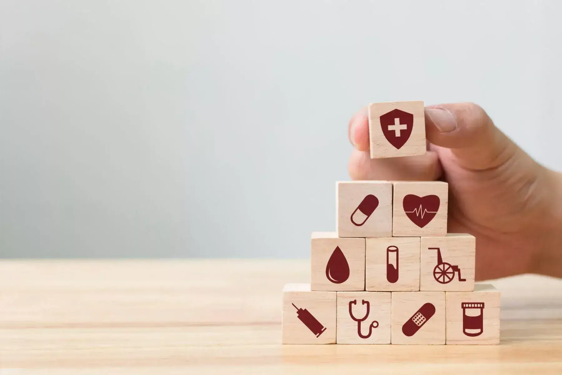 A hand stacking wooden blocks printed with healthcare icons into a pyramid.