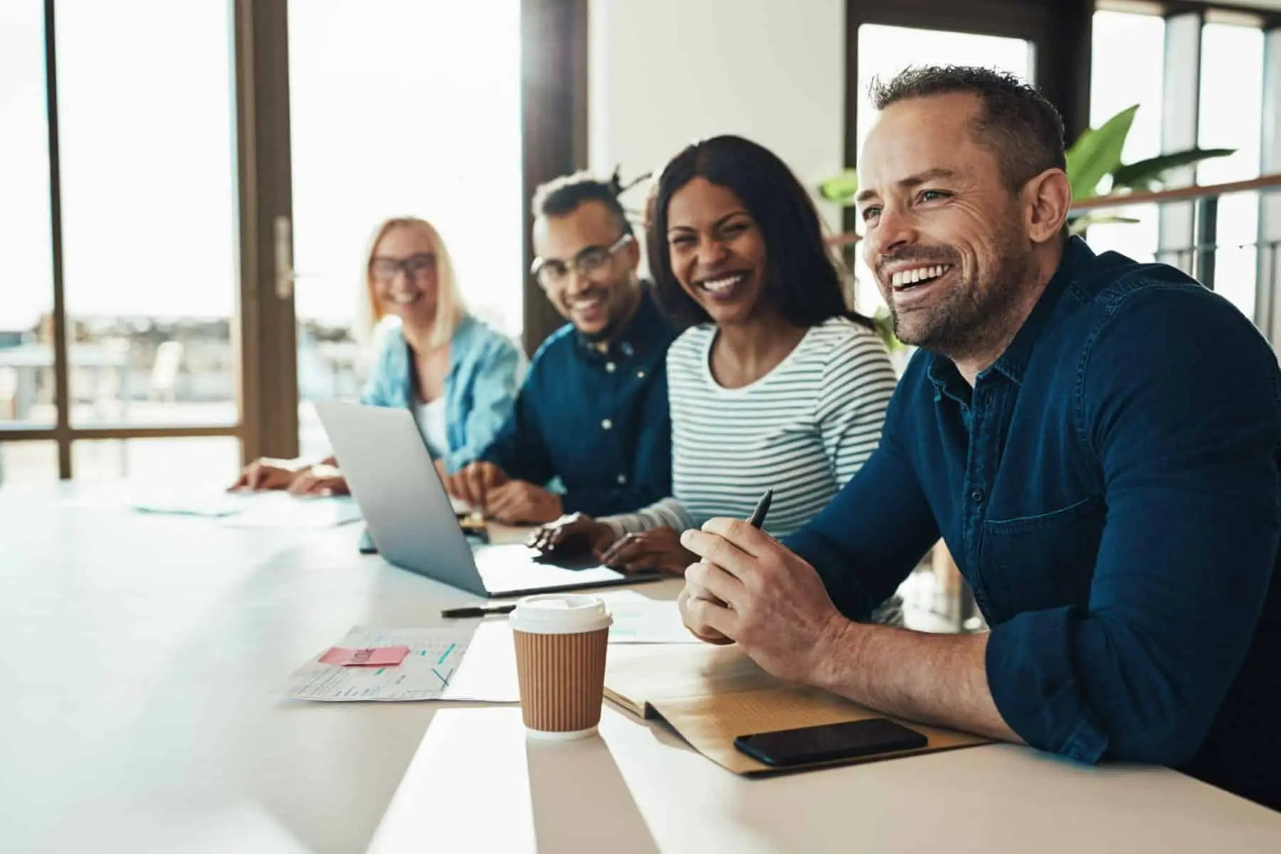 A group of smiling colleagues seated at a long table in a bright office.