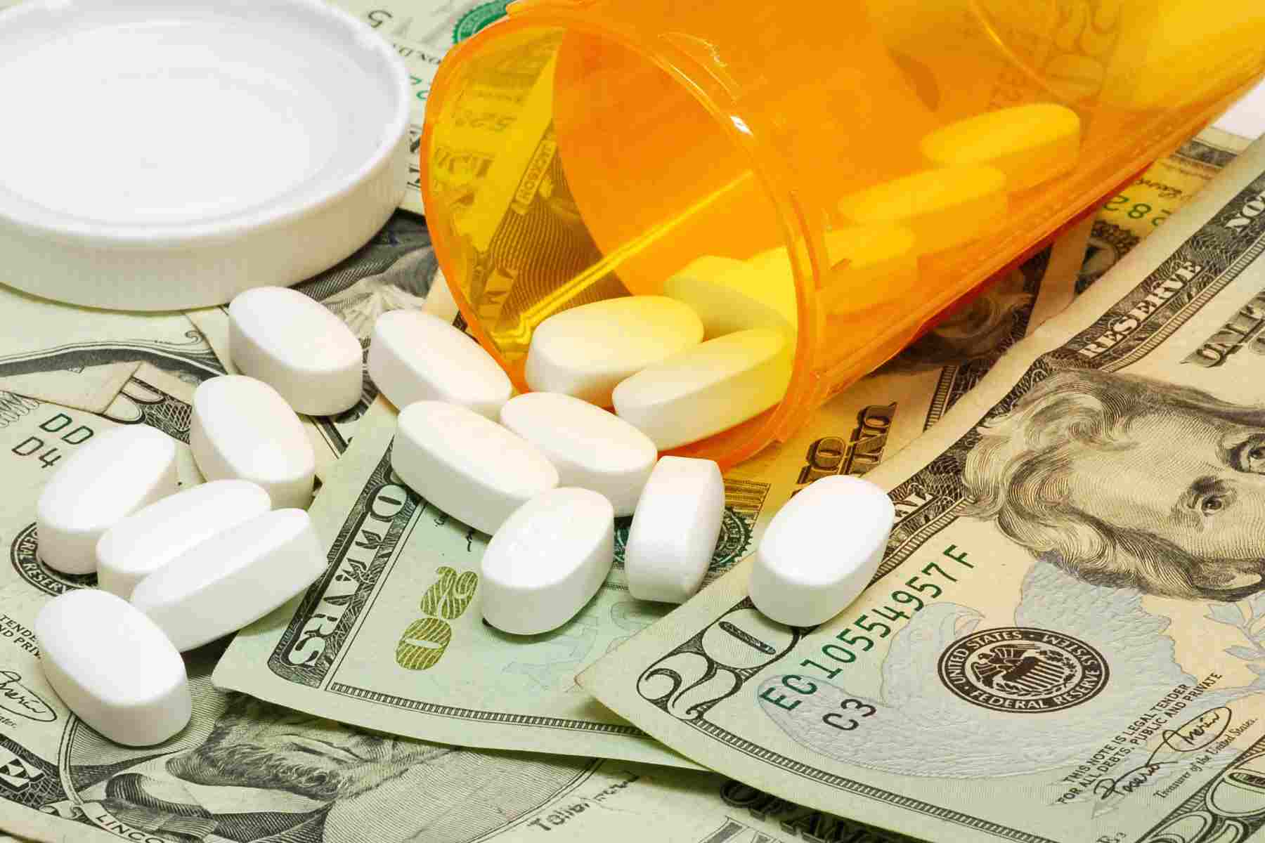White pills spilling from a prescription bottle onto U.S. currency, representing prescription drug costs.