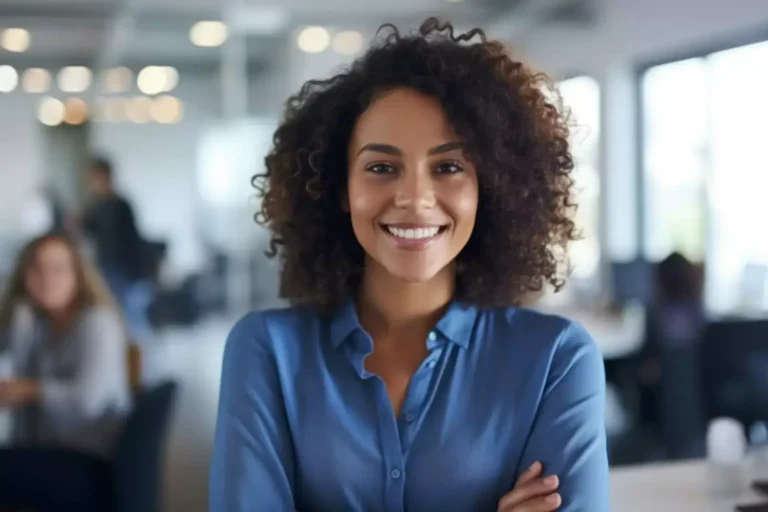 A smiling woman with curly hair and arms crossed standing in an office.