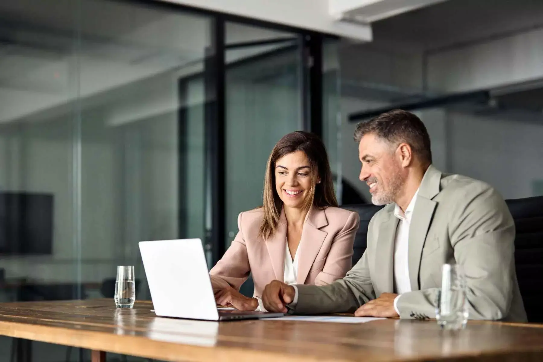 A businesswoman and businessman looking at a laptop together at a table.