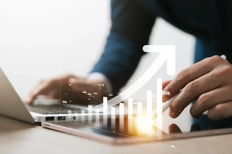A businessman working at a laptop with an upward arrow and bar graph overlay, representing growth.