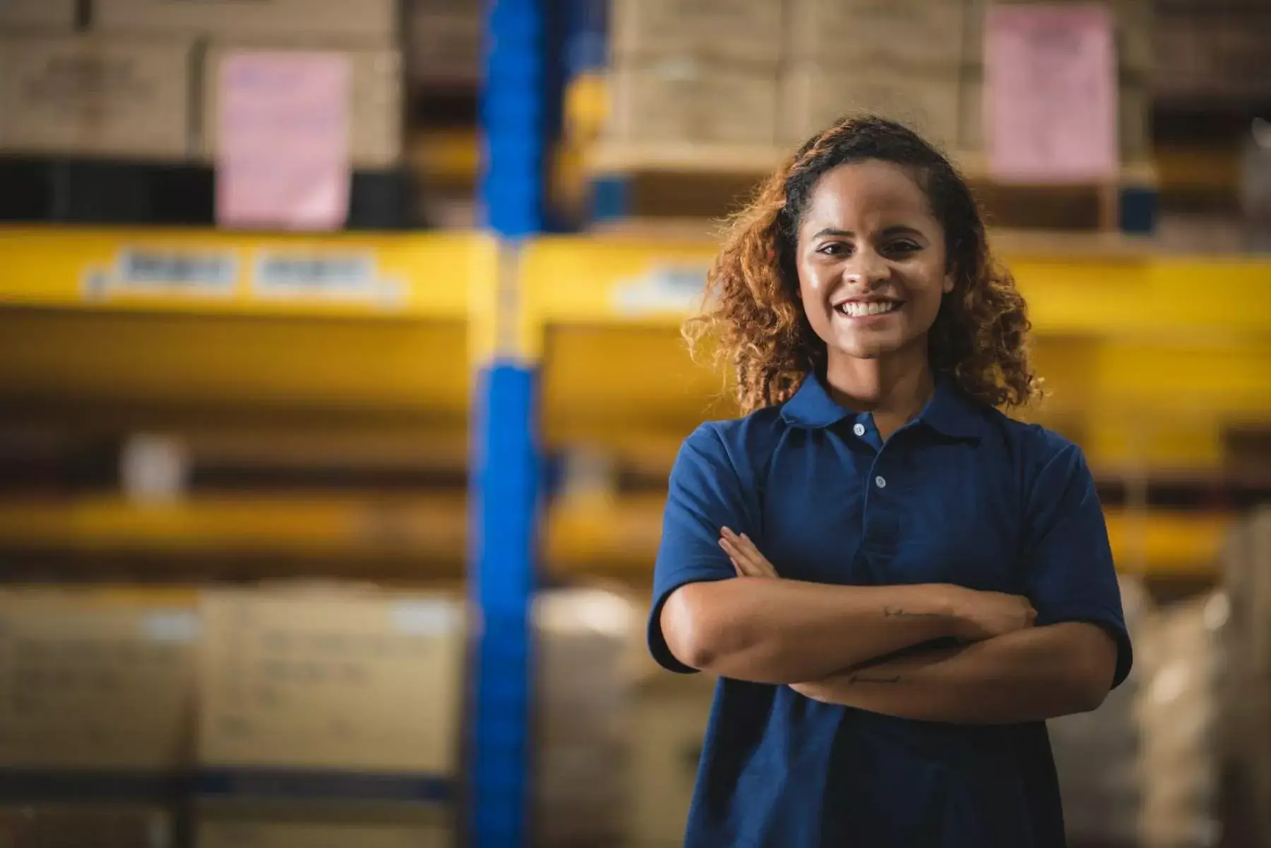 A smiling woman with arms crossed standing in a warehouse.