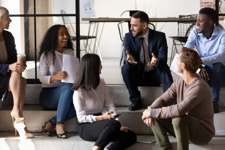 A diverse group of colleagues in an informal group discussion, one man gesturing.