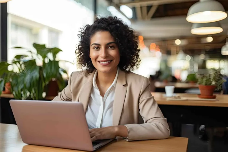 A smiling businesswoman working on a laptop in a modern workspace.
