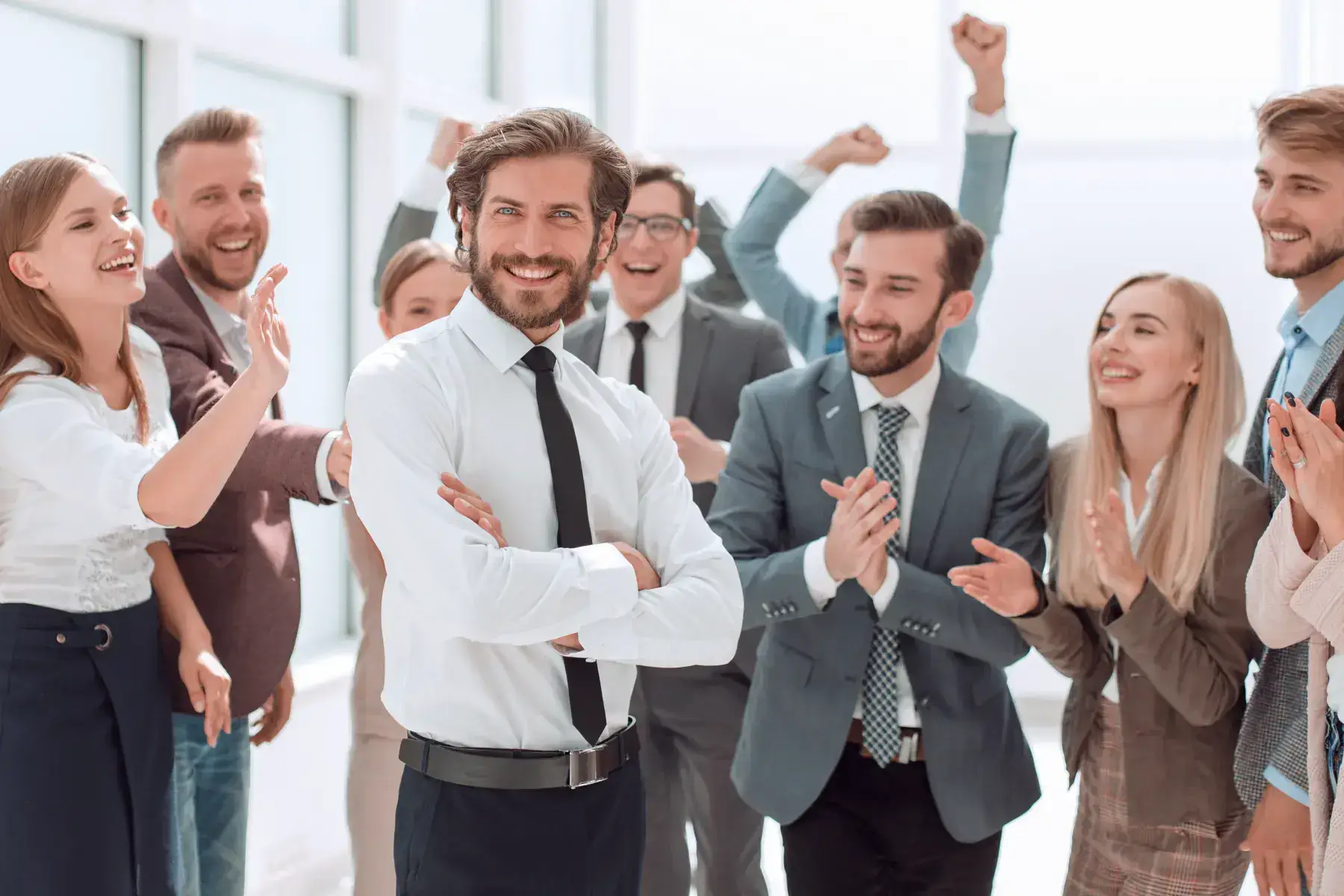 A businessman with arms crossed as colleagues celebrate and applaud behind him.