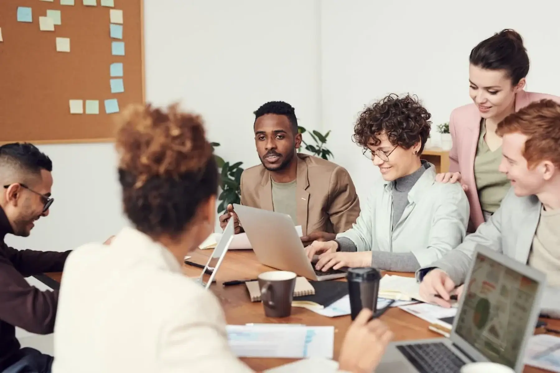 A diverse team collaborating around a table with laptops in a bright workspace.