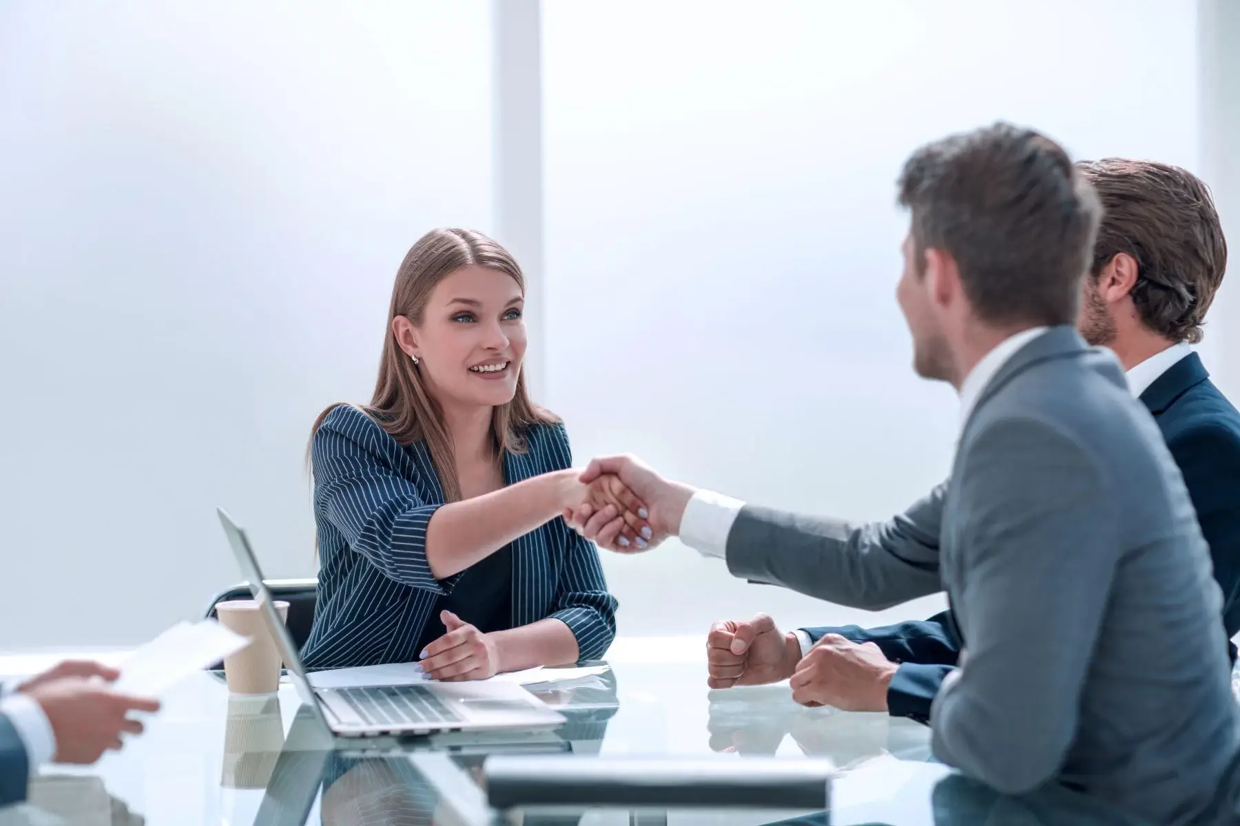 A woman shaking hands with a man across a desk during a business meeting.