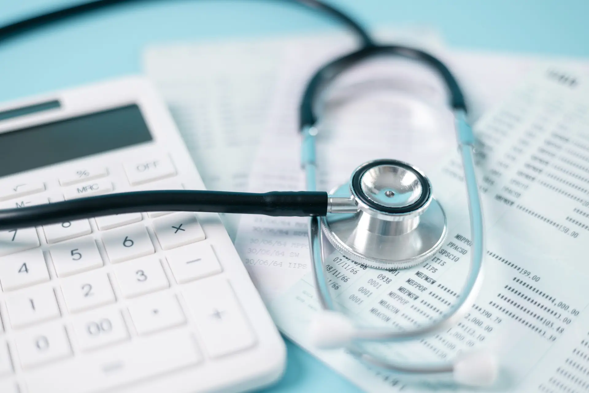 A stethoscope and calculator resting on medical billing paperwork, representing healthcare costs.