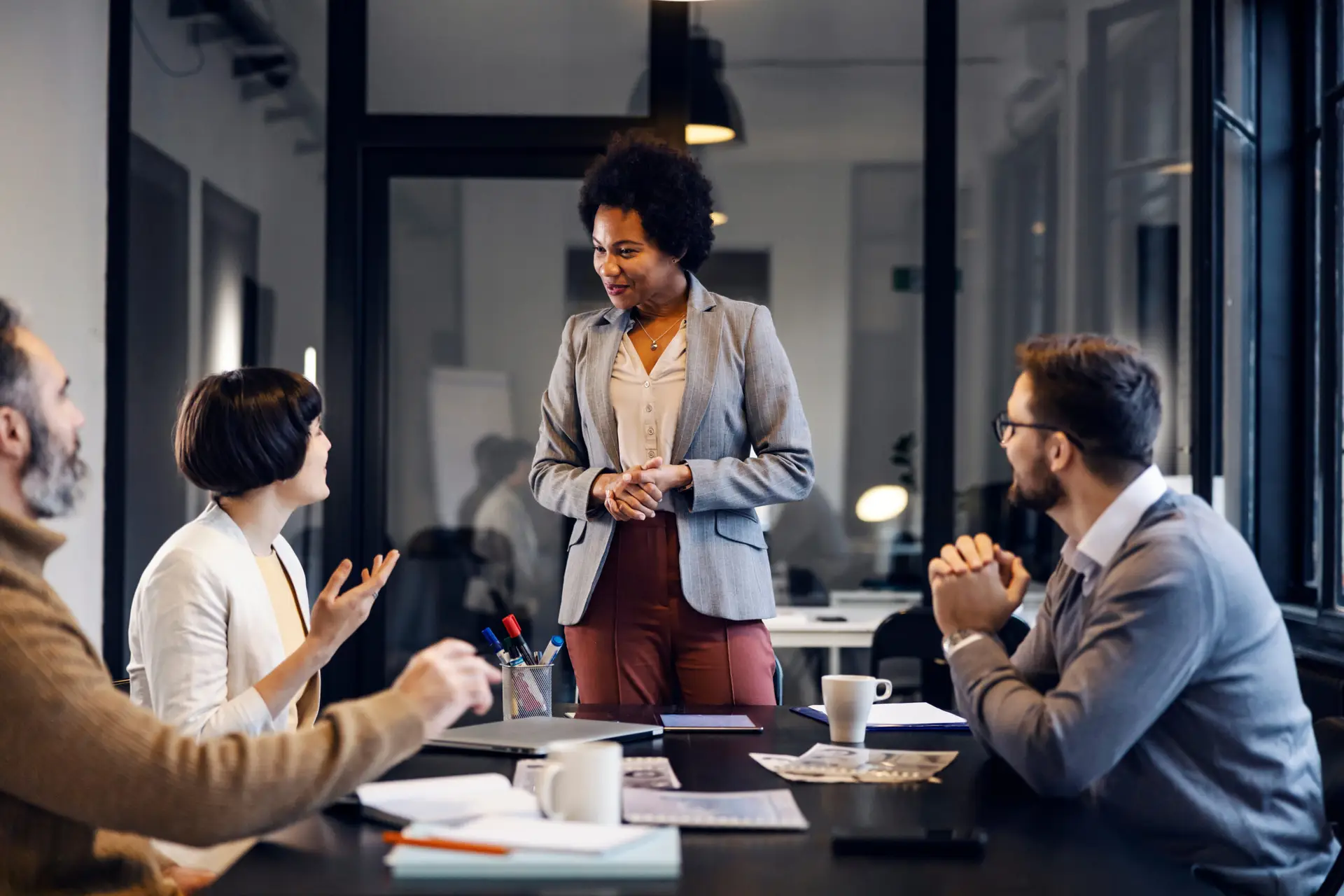A woman presenting to applauding colleagues during an office meeting.