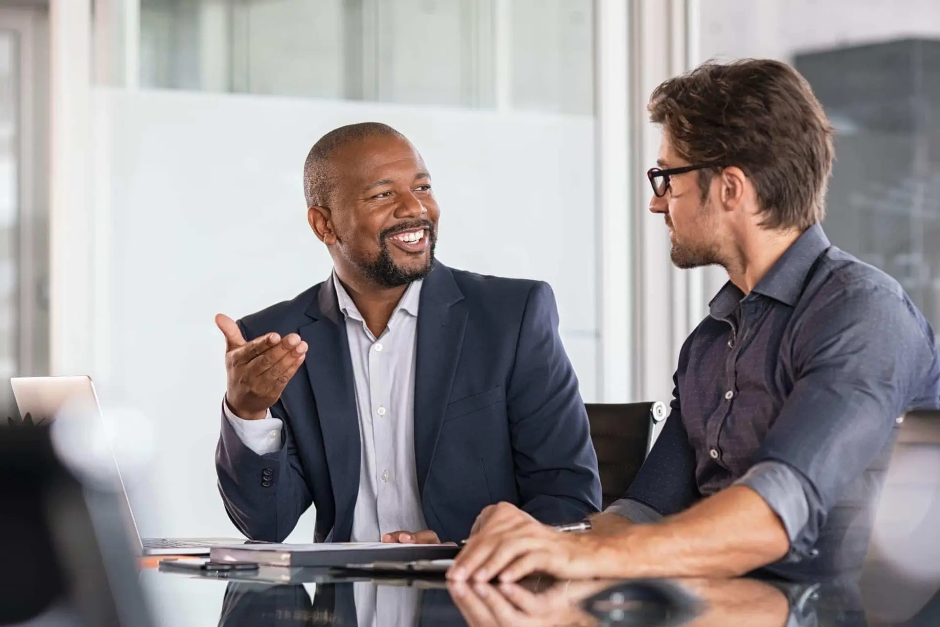 Two businessmen smiling and having a conversation at a table.