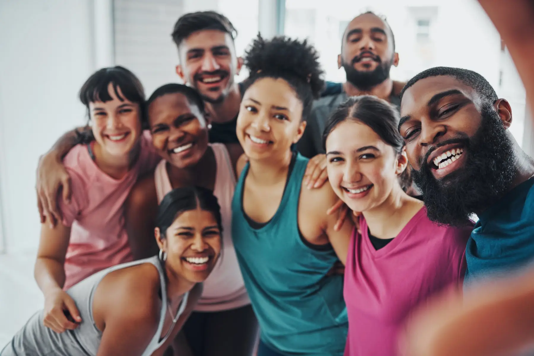 A diverse group of smiling people posing together for a group selfie after a workout.
