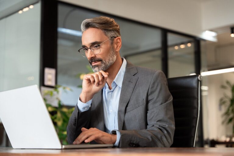 A businessman in a suit working thoughtfully at a laptop in an office.