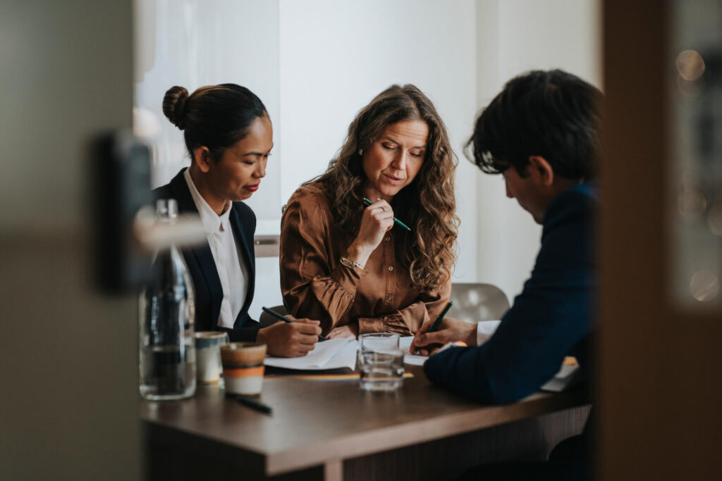 Three diverse professionals in business attire collaborating around a meeting table with documents and coffee cups