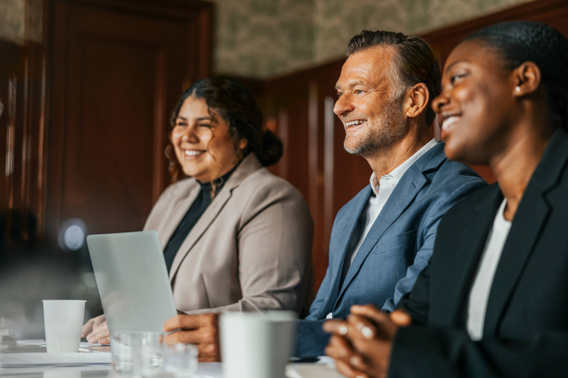 Three diverse business professionals smiling during a discussion at a meeting table