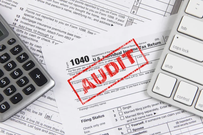 A 1040 tax form stamped Audit beside a calculator and keyboard.