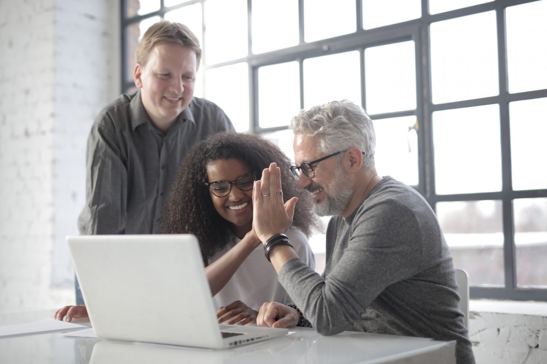 Three colleagues smiling around a laptop in a bright office.