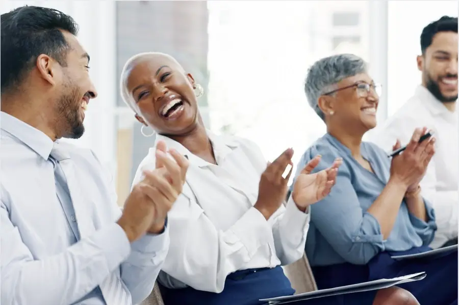 Diverse group of professionals laughing and clapping in a meeting