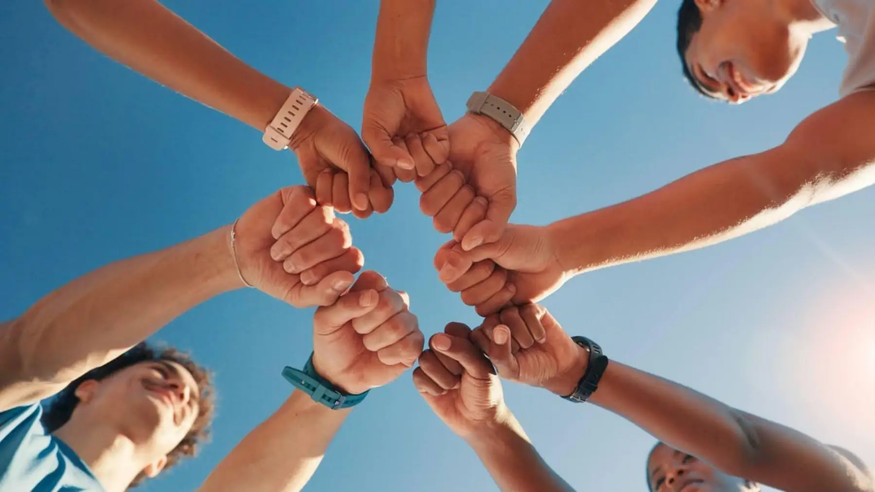 A diverse group joining their fists together in a circle under a bright sky, representing teamwork.