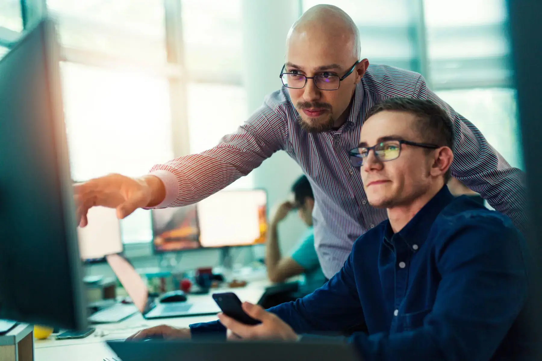 Two colleagues working together at a computer, one pointing at the screen.